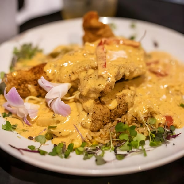 Crispy fried chicken covered in creamy sauce, served with rice, vegetables, and edible flowers.