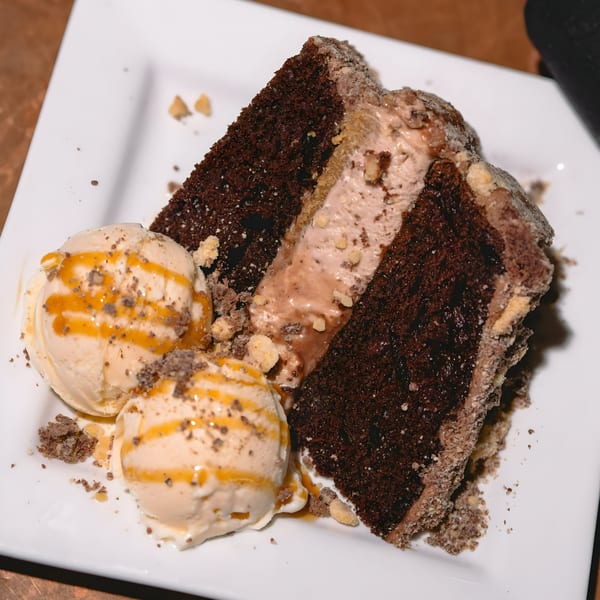 A slice of chocolate cake with creamy filling and two scoops of ice cream drizzled with caramel.
