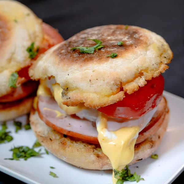 Two Noir Kitchen & Cocktails breakfast sandwiches with ham, egg, tomato, and hollandaise sauce.