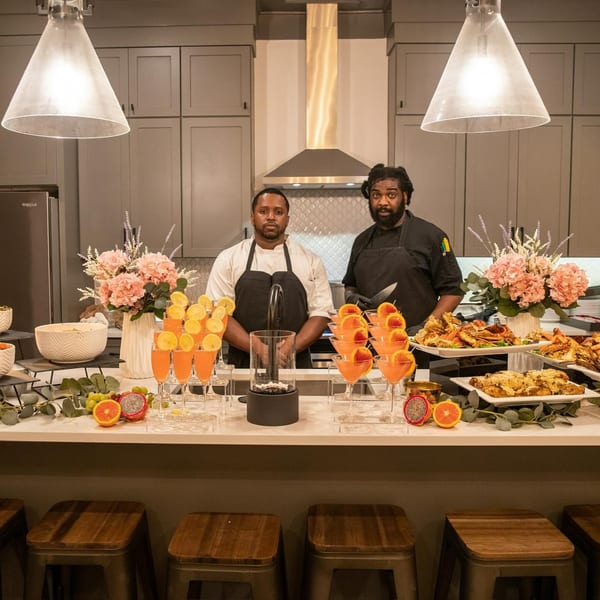 Two Noir Kitchen & Cocktails chefs behind a counter laden with soul food and cocktails.