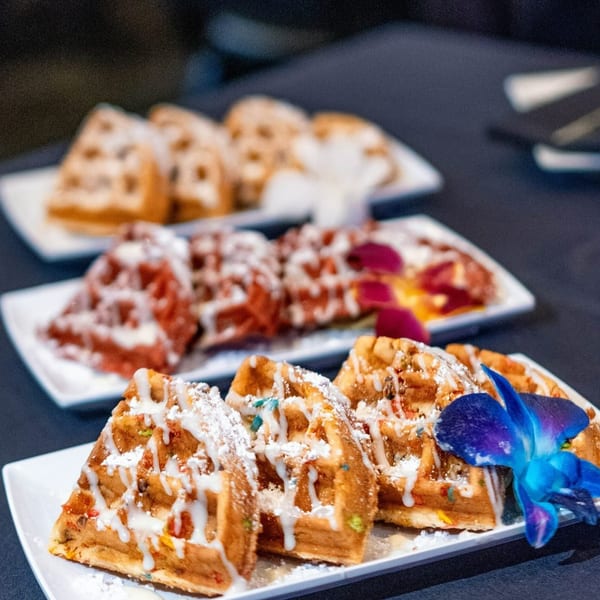 Plates of Noir Kitchen & Cocktails' waffles, drizzled with icing and powdered sugar, with a blue orchid.
