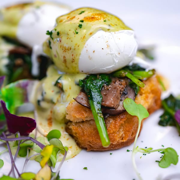 Poached eggs with hollandaise sauce, mushrooms, and greens on toast, garnished with microgreens.