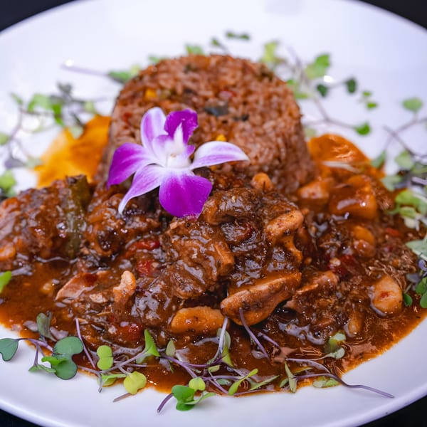 Oxtail stew with rice, garnished with microgreens and an orchid, on a white plate.