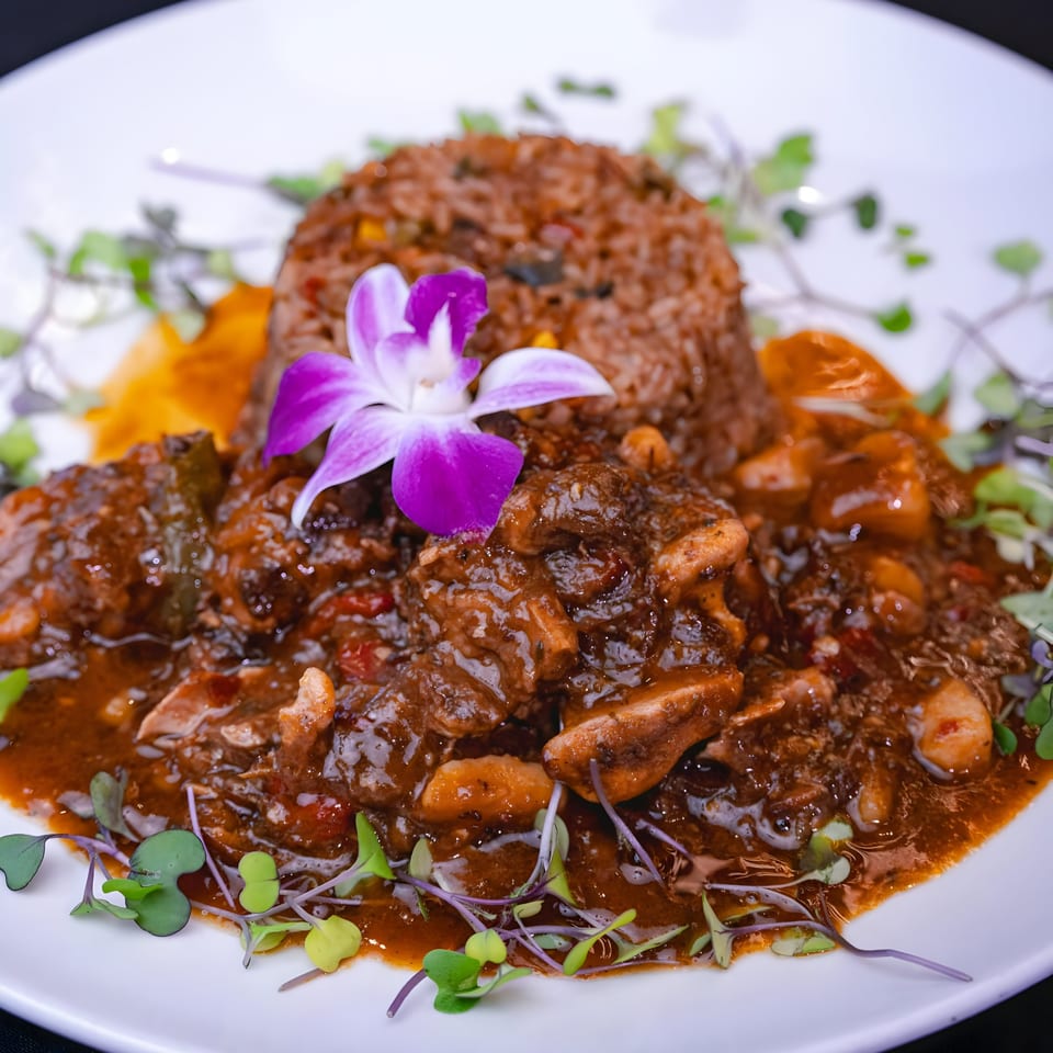 Oxtail stew with rice, garnished with microgreens and an orchid, on a white plate.