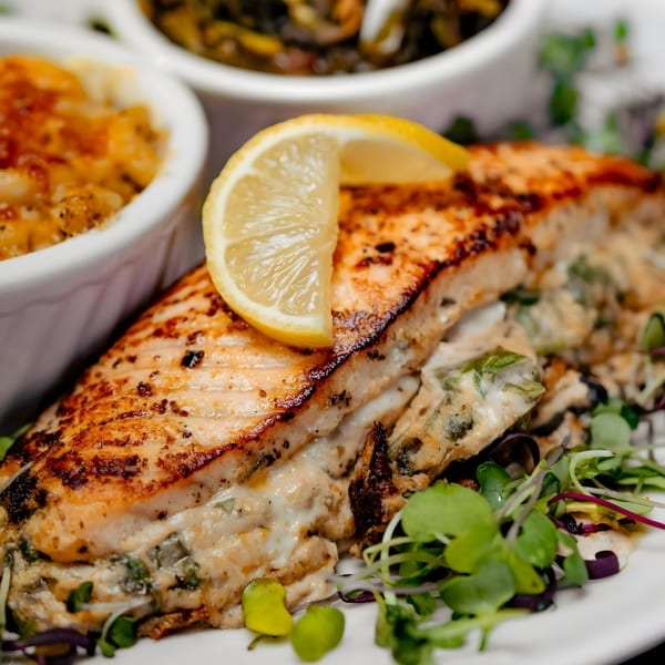 Grilled salmon with a lemon slice, served with macaroni and cheese and collard greens.